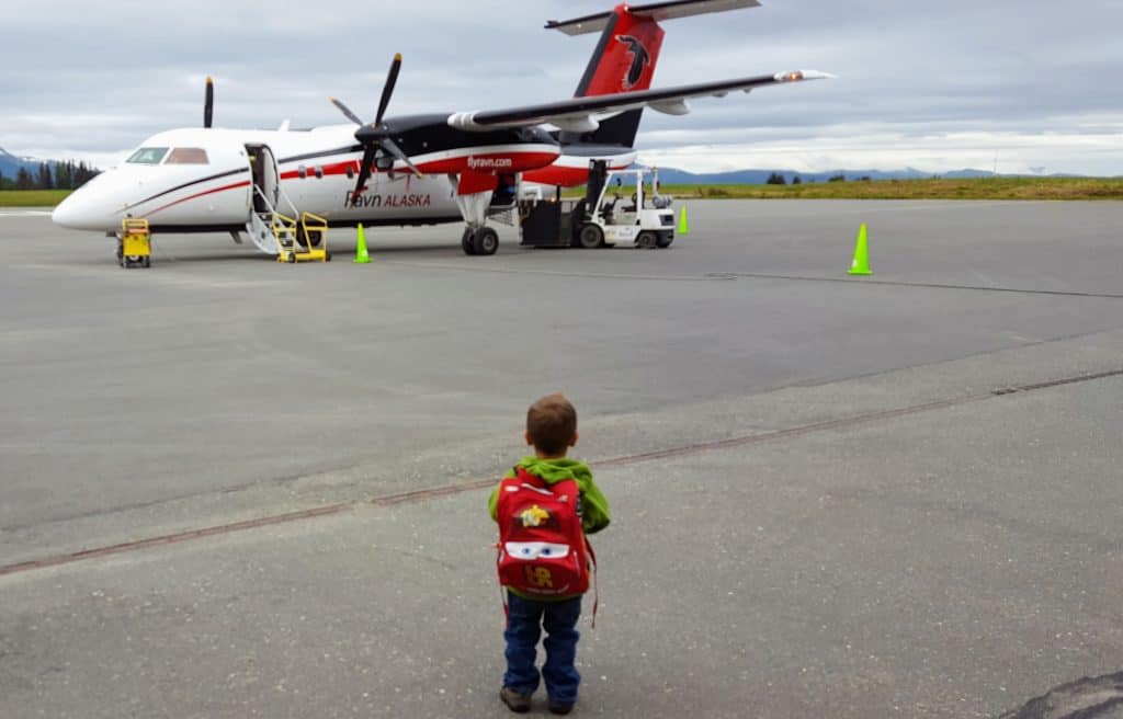 Eli standing in front of a twin prop airplane on the runway - traveling with an only child