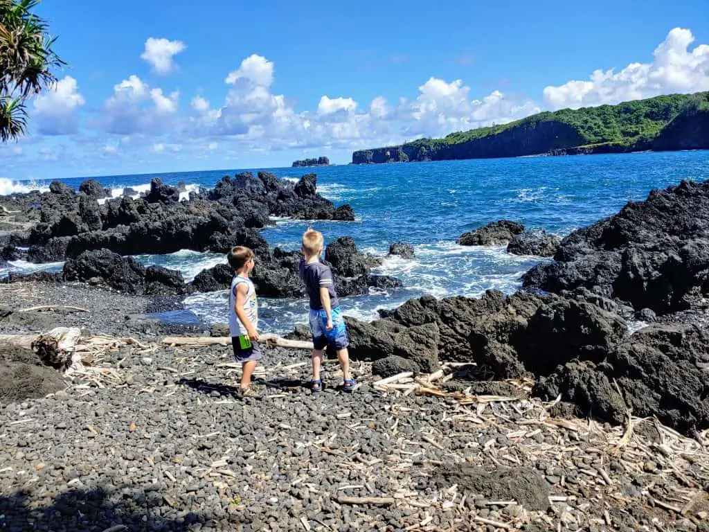 two boys throwing rocks into the ocean on the Keanae peninsula Maui