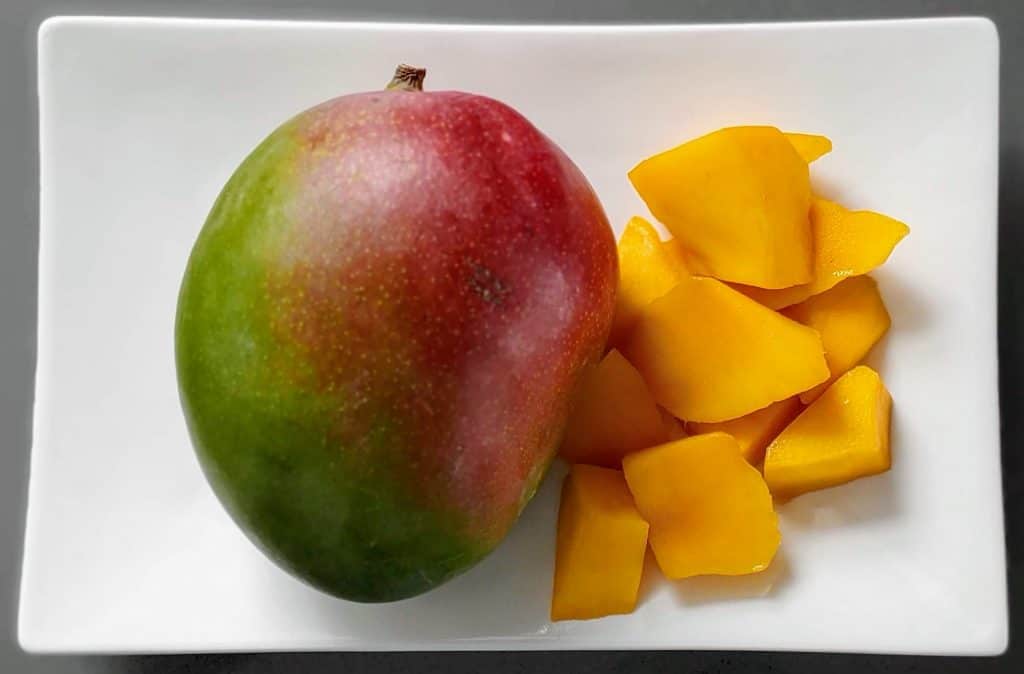 One whole mango and a mango sliced up on a white plate - Fruit in Hawaii