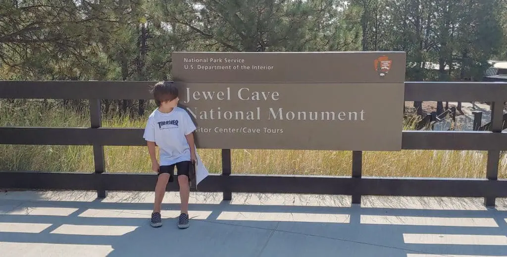 boy standing in front of the Jewel Cave National Monument sign in the black hills of south dakota