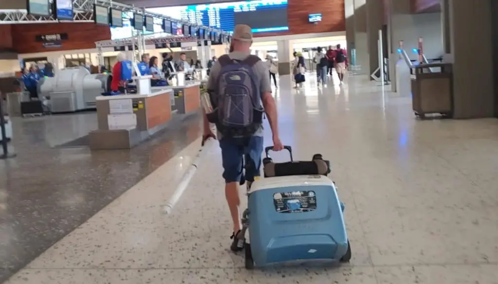 Man walking through the airport pulling a cooler on wheels as his checked luggage