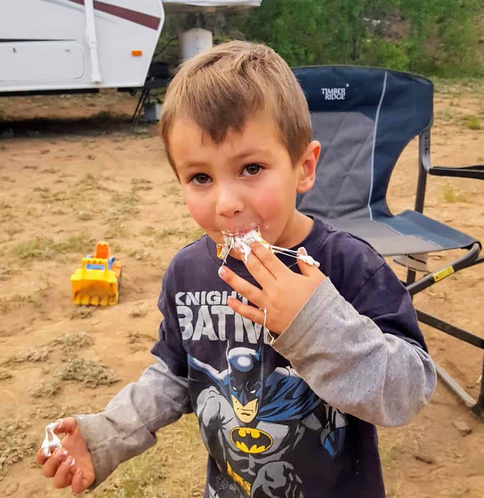 Little boy eating a roasted marshmallow with marshmallow all over his hands