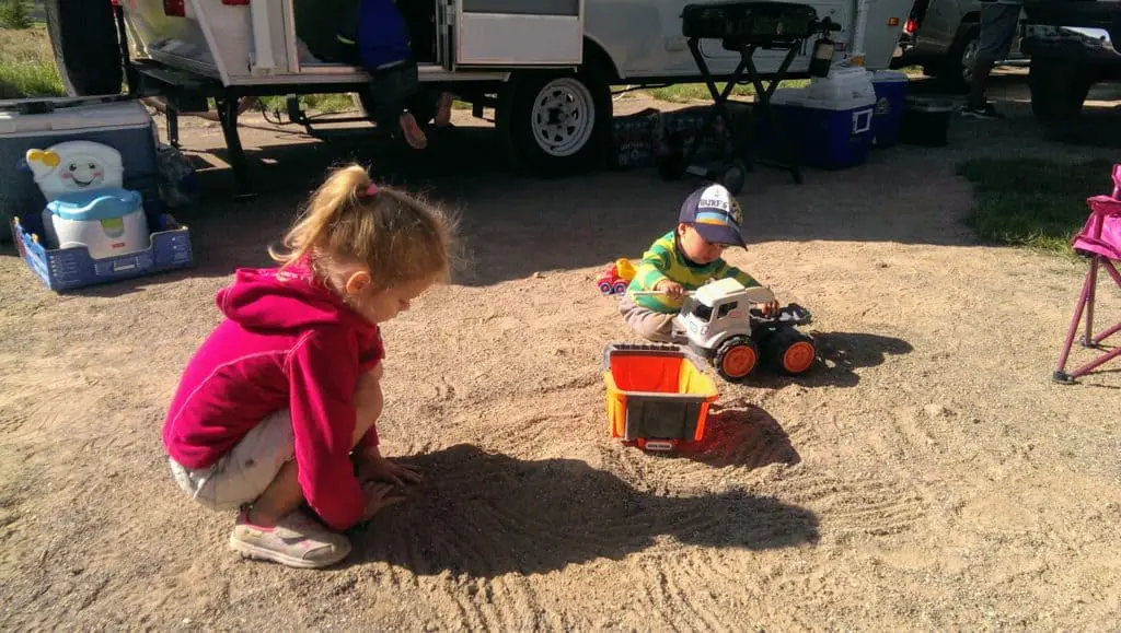Children playing in the dirt in front of a camper near a toddler potty chair one essential when camping with kids