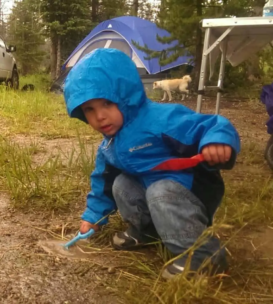 child playing with shovels in the mud wearing a rain jacket - an essential for camping with kids