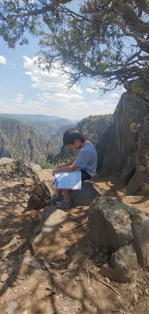 boy working in his Junior Ranger book under a tree at Black Canyon of the Gunnison National Park in Colorado