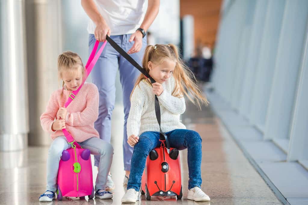 two kids on a ride-on suitcase in the airport, a great alternative to a stroller