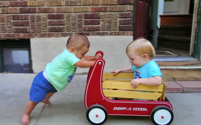 toddler pushing another toddler in a wagon