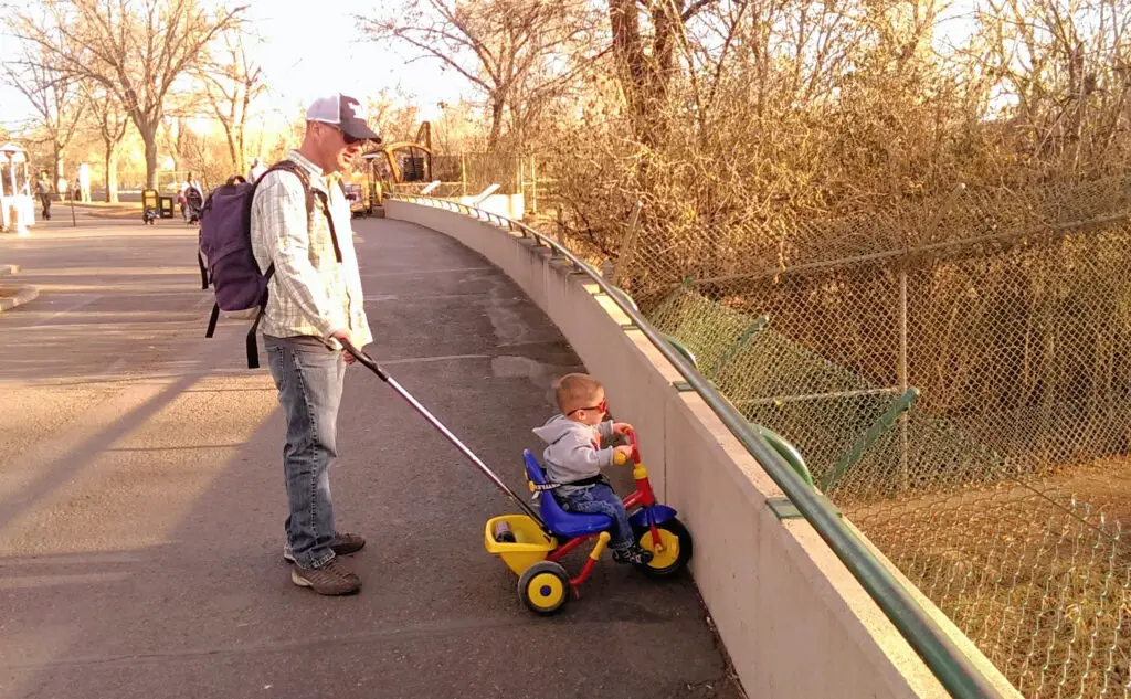 Man pushing a toddler on a tricycle with a handle