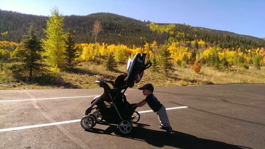 toddler pushing his stroller in the mountains with fall colors in the background
